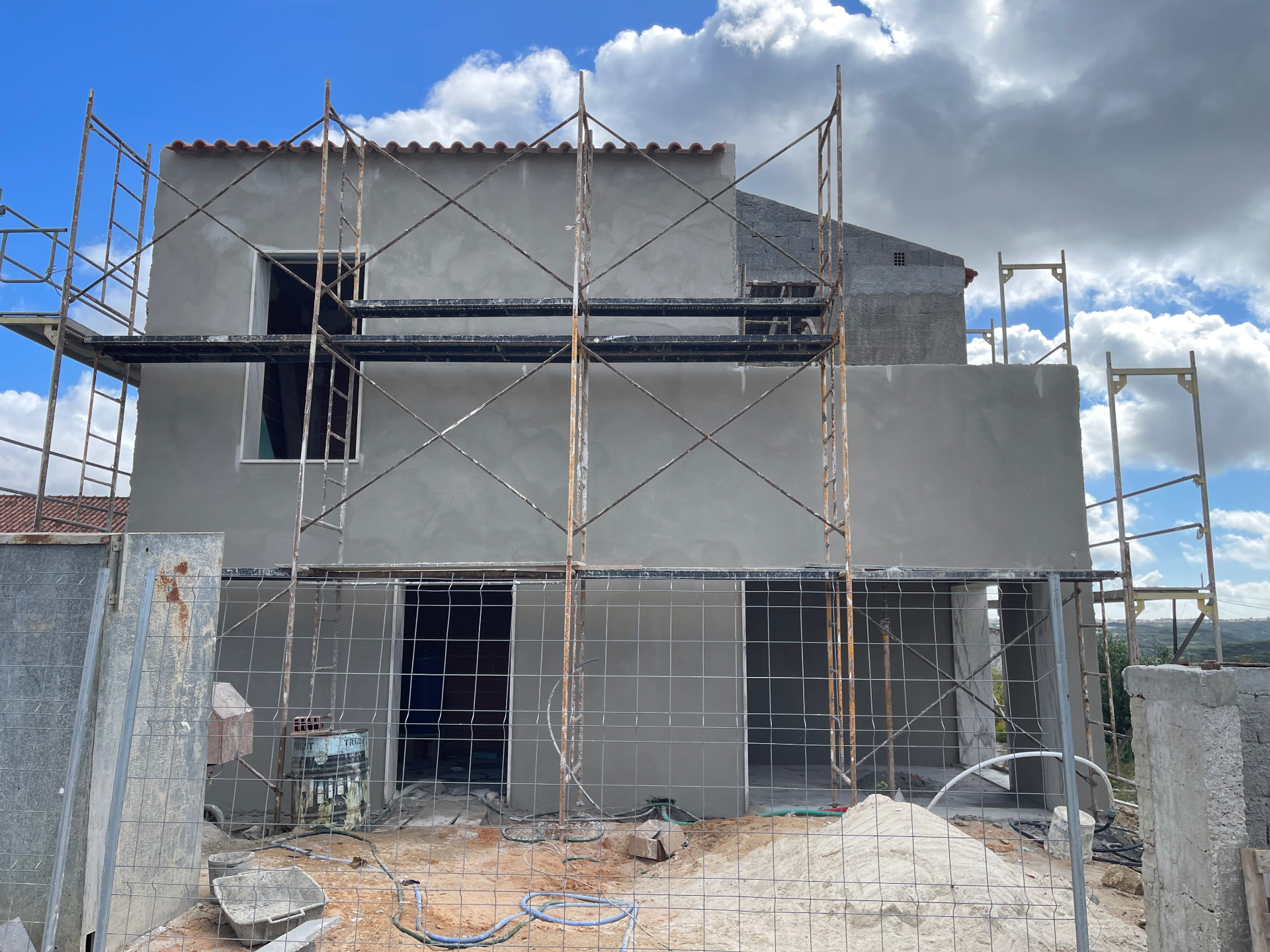 Fachada de moradia com reboco projetado aplicado e andaimes montados, em Montelavar